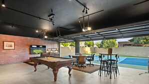 Une table de billard avec des chaises, un téléviseur et un mur en briques.