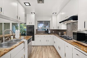 Een moderne keuken met witte kastjes, granieten aanrechtbladen en een tegelwand van baksteen.