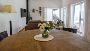 Un coin repas avec une table en bois, un vase de fleurs et une vue sur l’extérieur grâce à de grandes fenêtres.