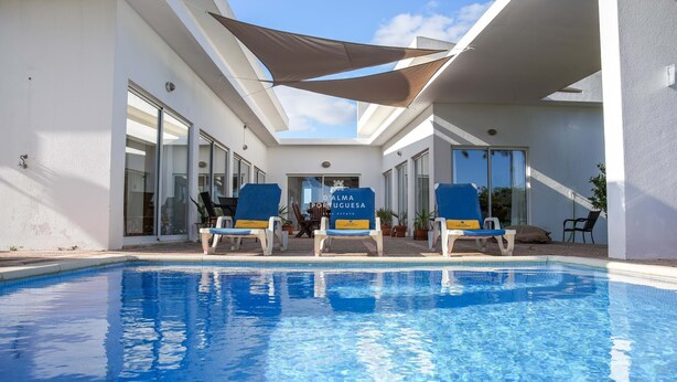 Une piscine avec des chaises longues, un espace ombragé et un panneau indiquant « ALMA PORTUGUESA ».