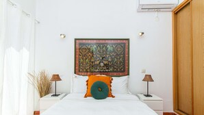Une chambre à coucher comprenant un lit, deux tables de chevet, une commode, une tête de lit ornée d’une tapisserie et une armoire en bois.