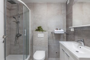 A modern bathroom with a glass shower enclosure, a white toilet, and a white sink. - Apartment in Croatia Near Stunning Coastline (Crikvenica)