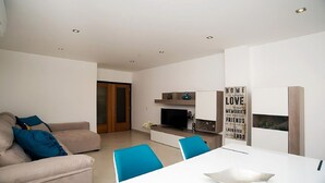 Ein modernes Wohnzimmer mit einer Couch, einem Fernseher und einem Esstisch mit Stühlen.
