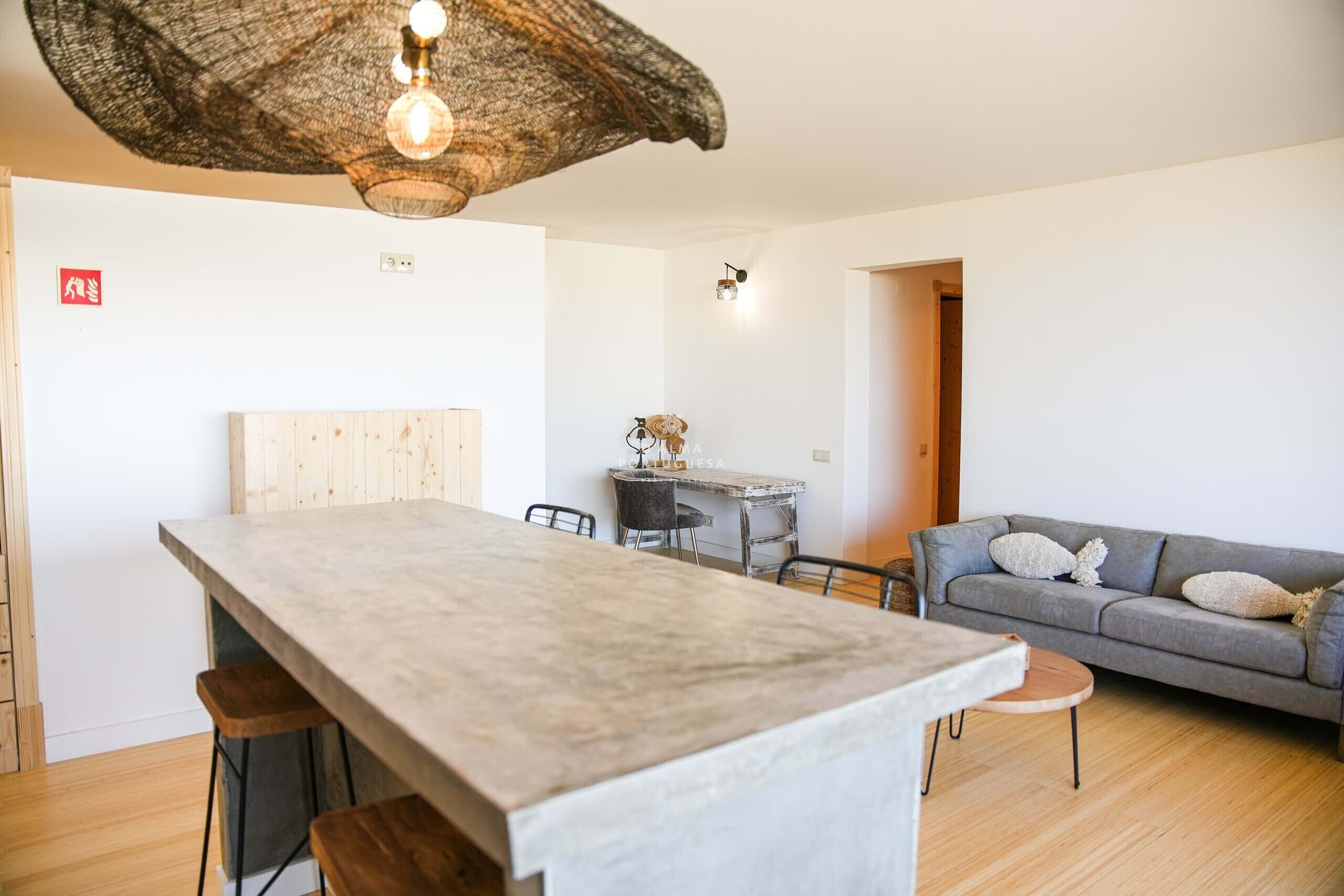 A modern living space with a central island, a grey sofa, and a dining area.
