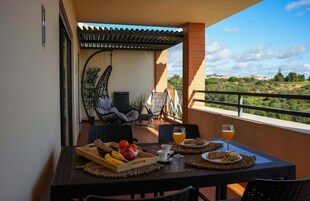 Varanda com mesa posta para o café da manhã, incluindo frutas, pão e bebidas.