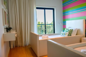 A hotel room with a bed, a window with curtains, a bedside table, and a colorful striped wall. - Apart Vilamoura Pine D'alma Portuguesa (Loulé)