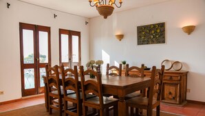 A dining area with a wooden table and chairs, a chandelier, and a decorative wall piece. - Apart Marina Boat View D`alma Portuguesa (Loulé)