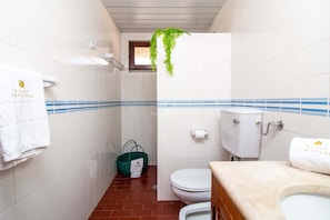 A bathroom with white tiled walls, a blue stripe, a white toilet, a sink, and a hanging plant. - Apart Marina Boat View D`alma Portuguesa (Loulé)