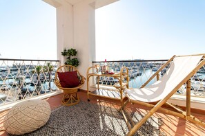A balcony with a wicker chair, a hammock, and a small table with a plant. - Apart Marina Boat View D`alma Portuguesa (Loulé)