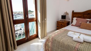 A hotel room with a bed, a nightstand, a lamp, and a view of boats through a window. - Apart Marina Boat View D`alma Portuguesa (Loulé)