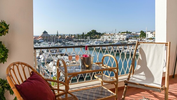 A balcony with wicker furniture, a white cloth, and a view of a marina with boats. - Apart Marina Boat View D`alma Portuguesa (Loulé)