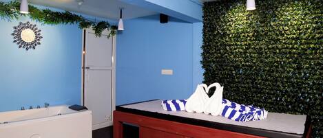A bathroom with a blue wall, a white bathtub, a red vanity, and a green leafy wall.
