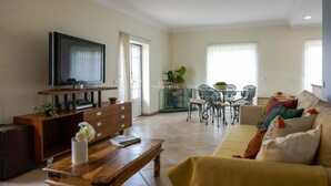 Een woonkamer met een televisie, houten meubels, een eethoek met stoelen en een bank.