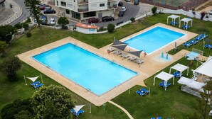 Zwei Pools mit Liegestühlen, ein Gebäude im Hintergrund und eine Straße mit Autos.