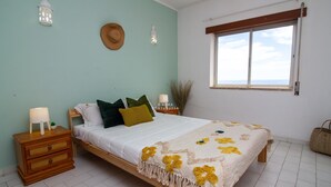 Ein Schlafzimmer mit Bett, Nachttisch, Fenster und Blick zum Himmel.