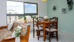 Ein Wohnzimmer mit einer Couch, einem Esstisch mit Stühlen, einem großen Fenster und Blick auf Gebäude.