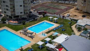 Un hotel con una piscina grande, varias zonas de descanso y un estacionamiento.