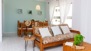Un salón acogedor con un sofá de madera, una mesa de comedor con sillas y una pequeña mesita con una planta.