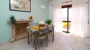 A dining area with a brick fireplace, a table with chairs, a framed painting, and a view through a door to an outdoor seating area. - Apart Anis Estrelado D´alma Portuguesa (Silves)