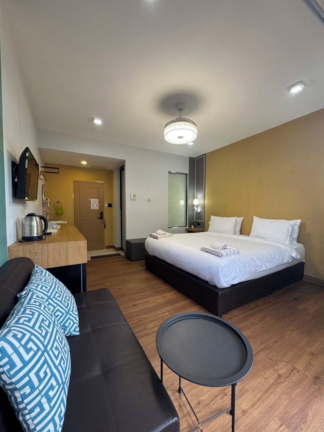 A hotel room with a bed, a small table, a sofa, and a kitchenette area.