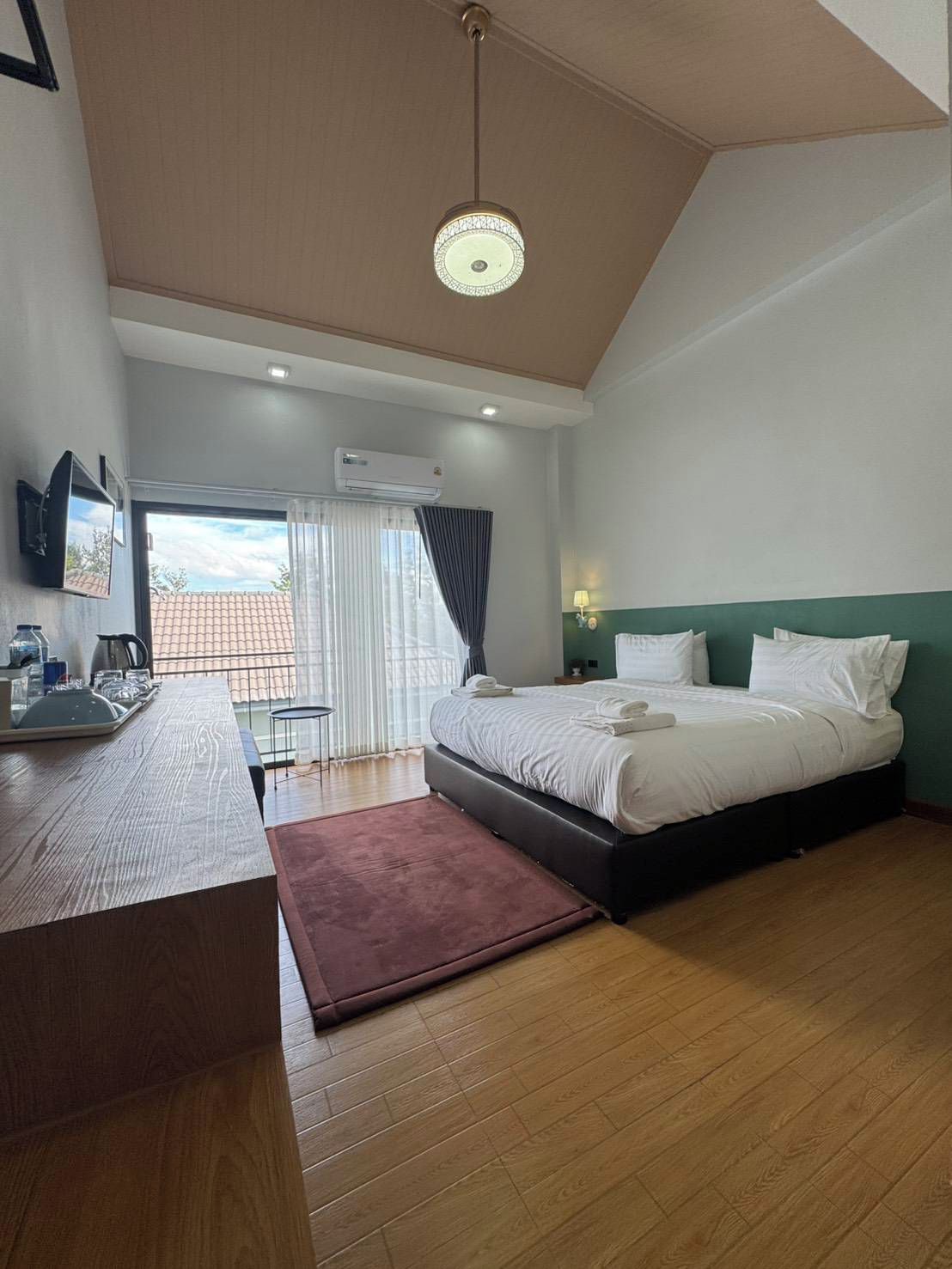 Una habitación de hotel moderna con suelo de madera, cama con ropa blanca, escritorio con televisor de pantalla plana y ventana con cortinas.