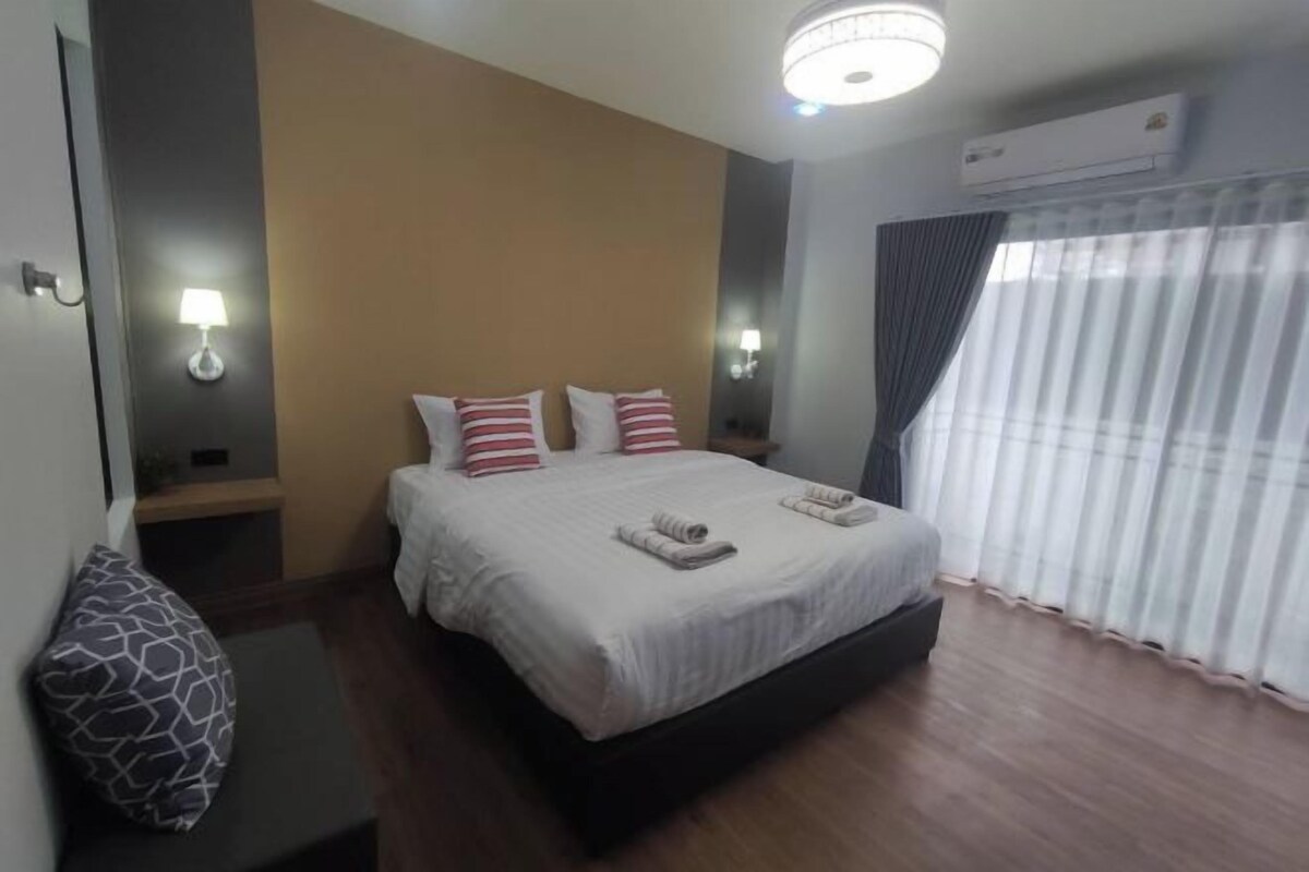A hotel room with a large bed, two bedside tables, a wall-mounted lamp, and a window with curtains.