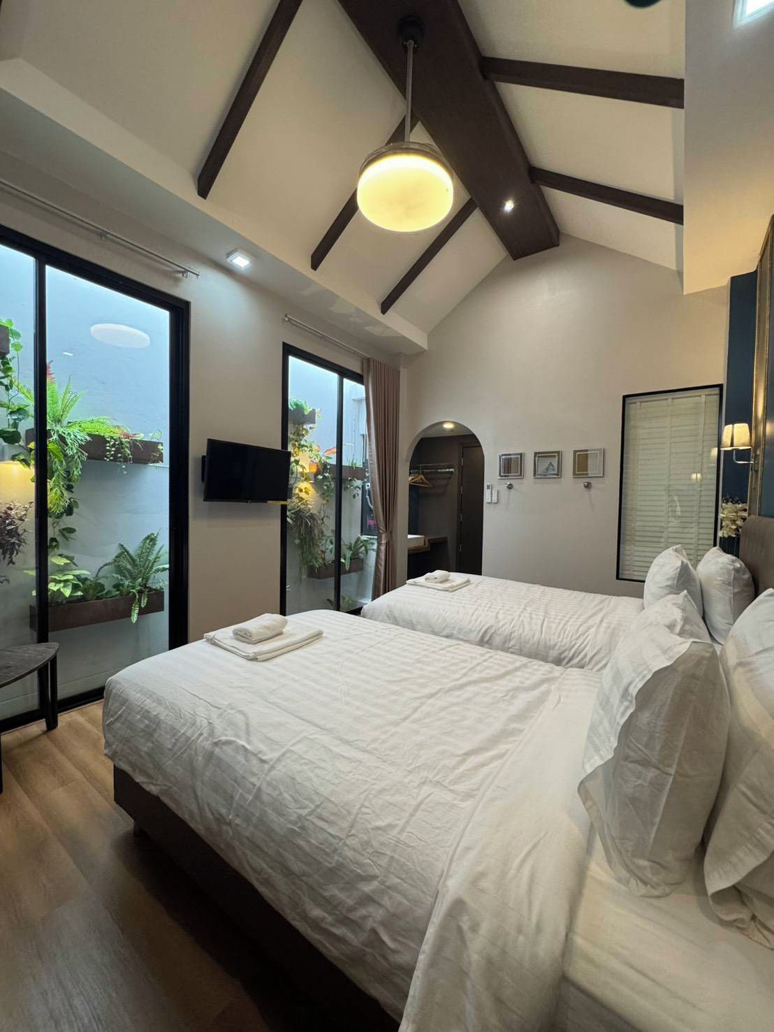 A modern bedroom with a large bed, a TV, and a view of greenery outside.
