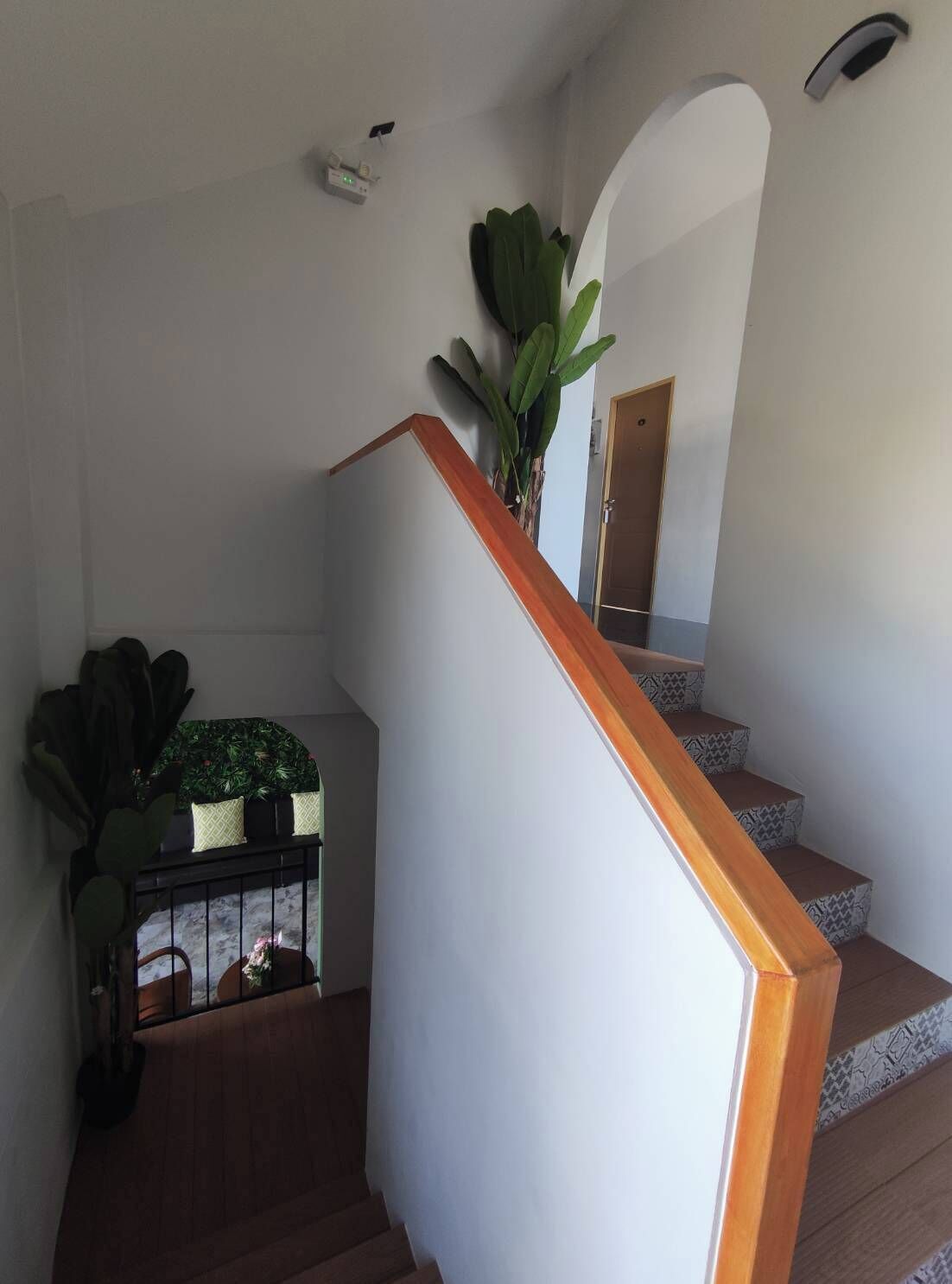 A staircase with wooden steps and a white handrail, leading to a landing with a potted plant and a small table with a plant on it.