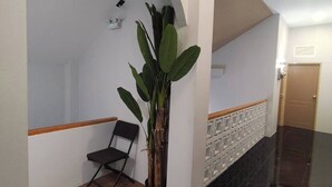 A hallway with a wooden floor, a black tiled section, a white wall with a decorative panel, and a potted plant. - U-SABAI VILLA  (Yasothon)