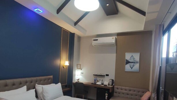 A hotel room with a large bed, a desk, a chair, a sofa, and an air conditioning unit. - U-SABAI VILLA  (Yasothon)