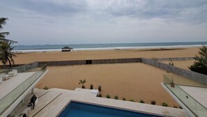 Vista de la playa desde un resort con piscina, una cabaña playera y palmeras.