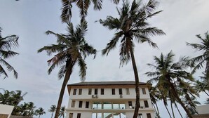 Un hotel frente a la playa con una estructura de dos pisos, palmeras y una playa de arena.