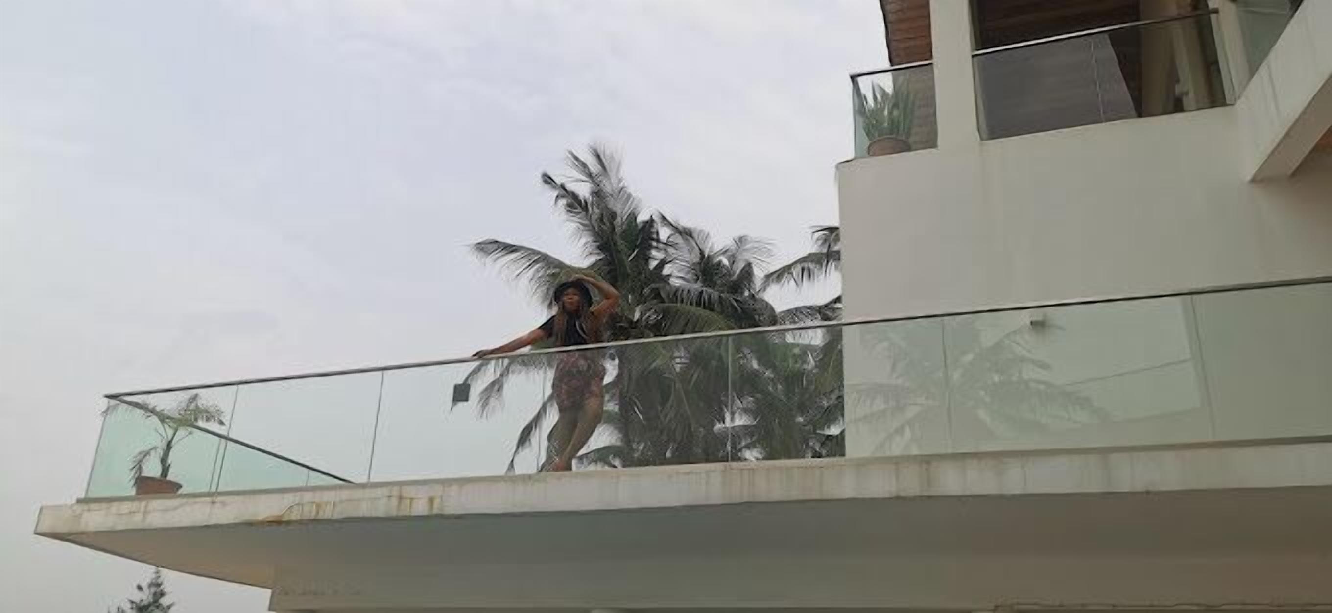 A balcony with a glass railing overlooking palm trees.