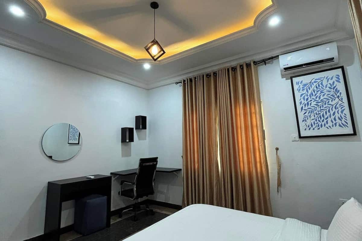 A hotel room with a bed, desk, chair, and a ceiling light fixture.