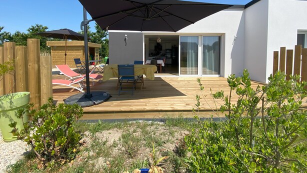 A modern outdoor patio with a wooden deck, a covered seating area, and a sliding glass door leading to an interior space. - Seaside house Loctudy (Loctudy)