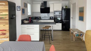 A modern kitchen with white cabinets, a black refrigerator, and a dining area with a table and chairs. - Seaside house Loctudy (Loctudy)