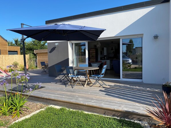 Une maison moderne dotée d’un patio comprenant une table et des chaises, un grand parasol et une vue sur la cuisine.