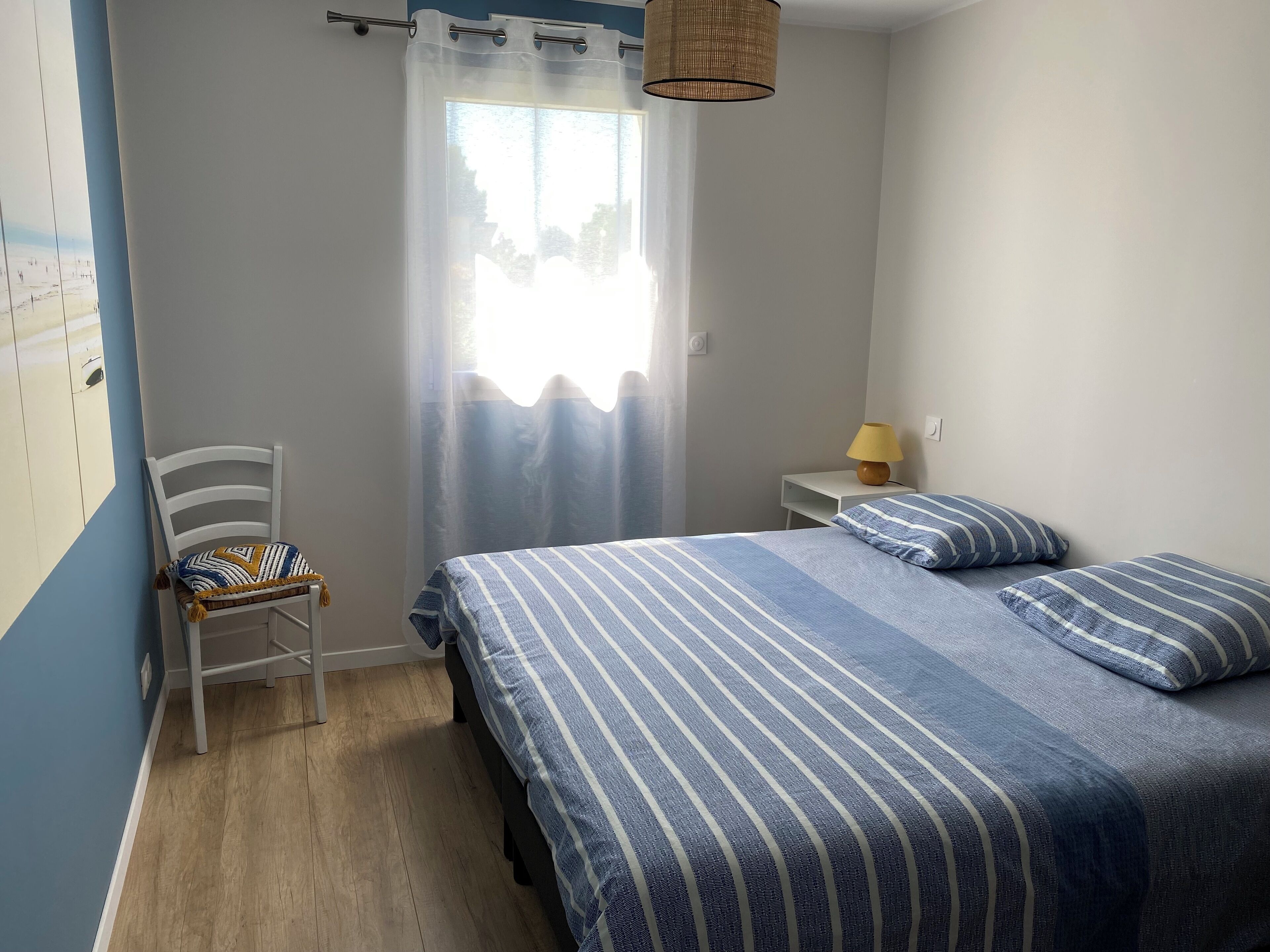A bedroom with a bed, a chair, a nightstand, a lamp, and a window with curtains.
