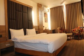 A hotel room with a large bed, wooden headboard, a desk with a chair, and a window with curtains.