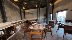 Ein Restaurant mit Holztischen und -stühlen, einer Ziegelwand und Blick auf die Stadt durch große Fenster.