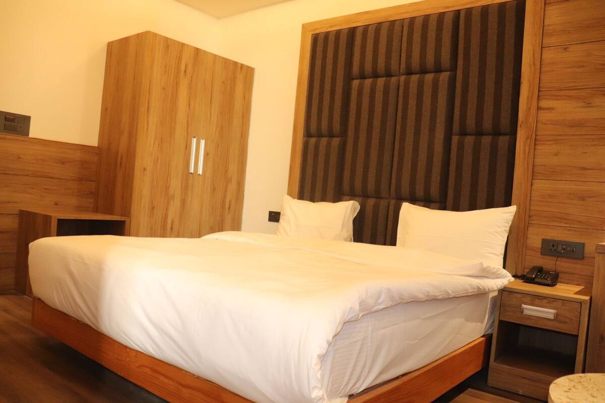 A bedroom with a wooden bed frame, a large wardrobe, and a bedside table with a phone.
