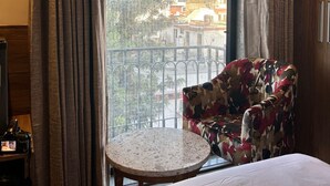 Ein Hotelzimmer mit einem Bett, einem runden Tisch, einem blumigen Sessel und einem großen Fenster mit Vorhängen.
