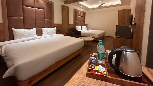 Ein Hotelzimmer mit zwei Betten, einem kleinen Tisch mit Wasserkocher und Snacks sowie einem an der Wand montierten Fernseher.
