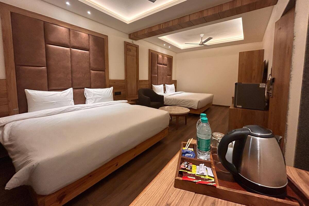 A hotel room with two beds, a small table with a kettle and snacks, and a TV mounted on the wall.