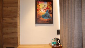 Ein Hotelzimmer mit einer Holzvertäfelung, einem gerahmten Gemälde einer Frau in einem blauen Kleid und einem Holztischchen mit Wasserkocher und Flaschen.