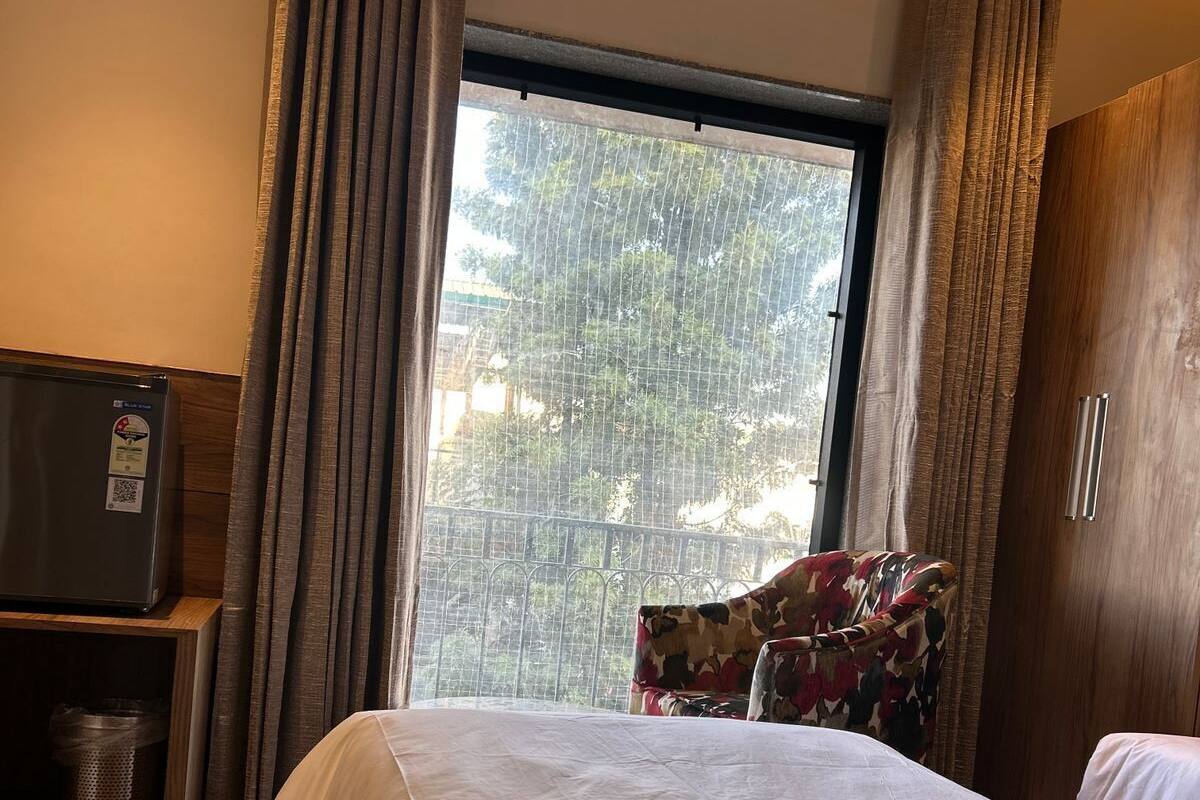 A hotel room with a bed, a TV, a chair, and a window with curtains.
