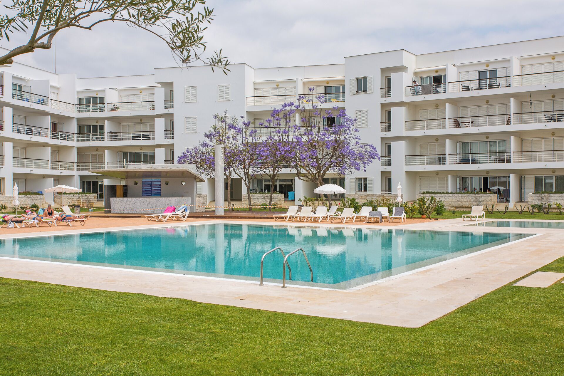 Et moderne hotel med en central swimmingpool omgivet af liggestole og parasoller.