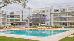 A modern hotel with a central swimming pool surrounded by lounge chairs and umbrellas. - Fantastic Tranquil Apartment by the Pool (Lagos)
