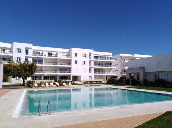 Un immeuble moderne à plusieurs étages, doté de balcons, d’une piscine et d’une pelouse bien entretenue.