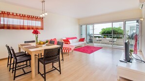 A modern living room with a dining area, a sofa, a TV, and a balcony with outdoor furniture. - Fantastic Tranquil Apartment by the Pool (Lagos)